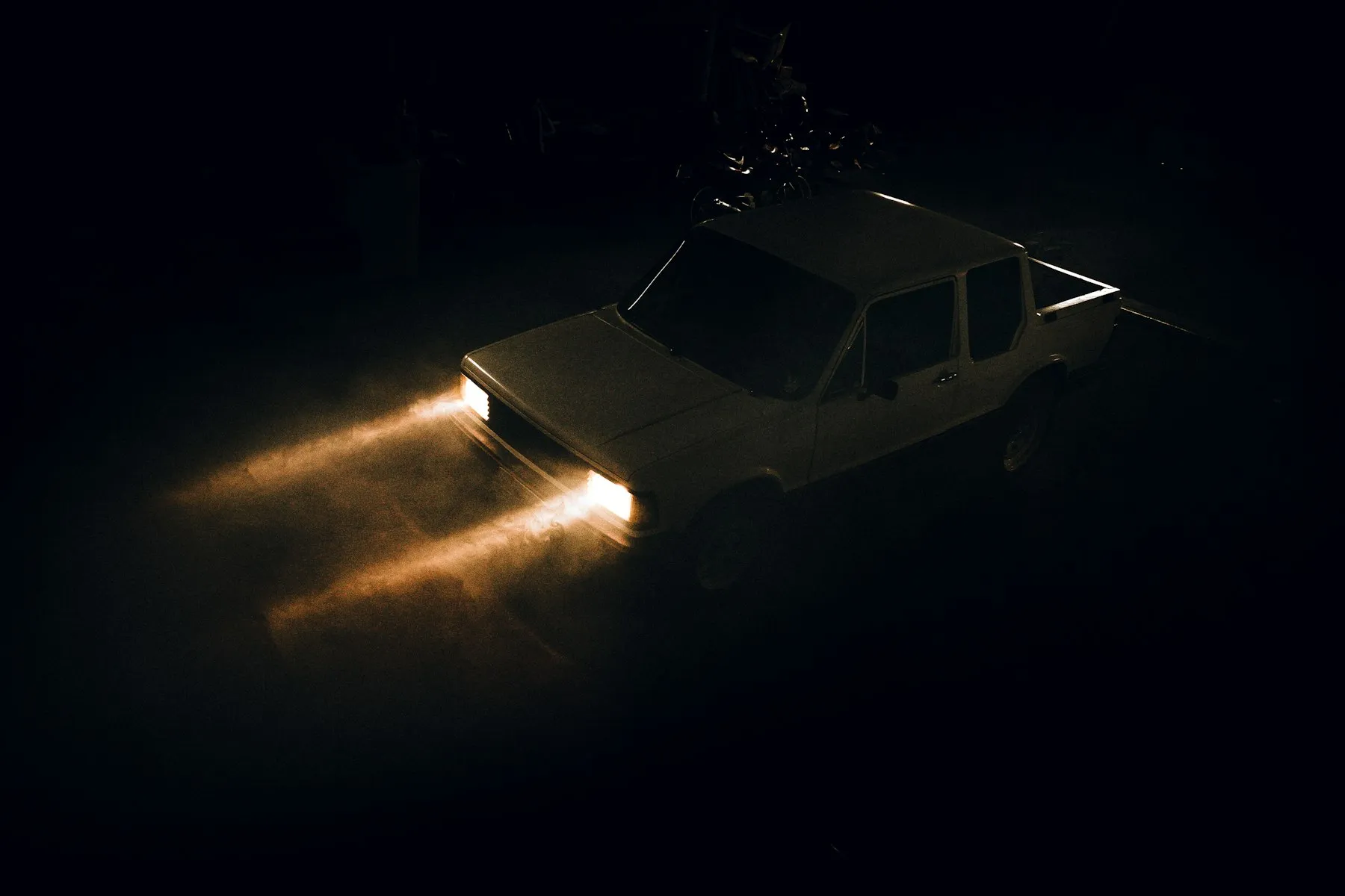 A vehicle on a dark road at night with its headlights cutting through the dust
