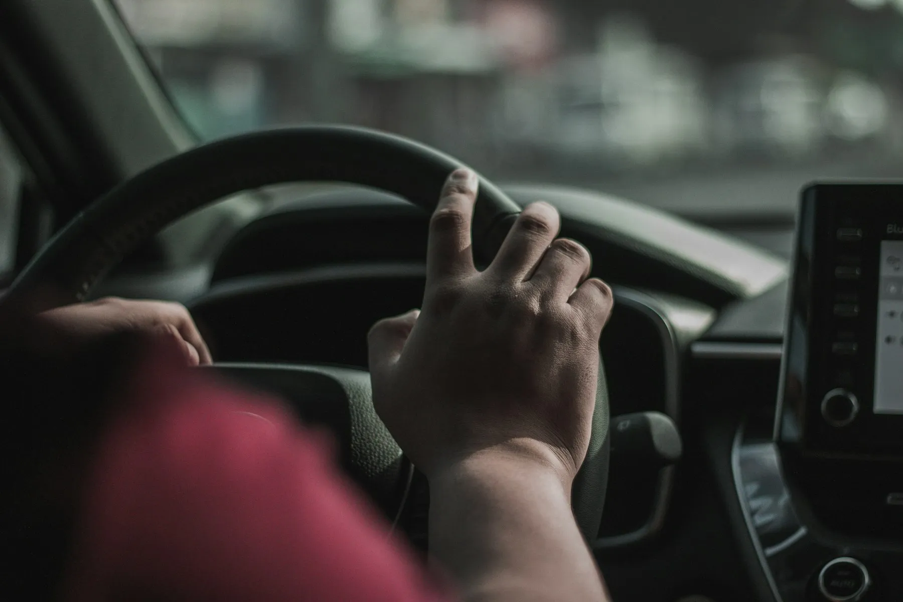 Driver with a hand on the steering wheel looking through the windshield