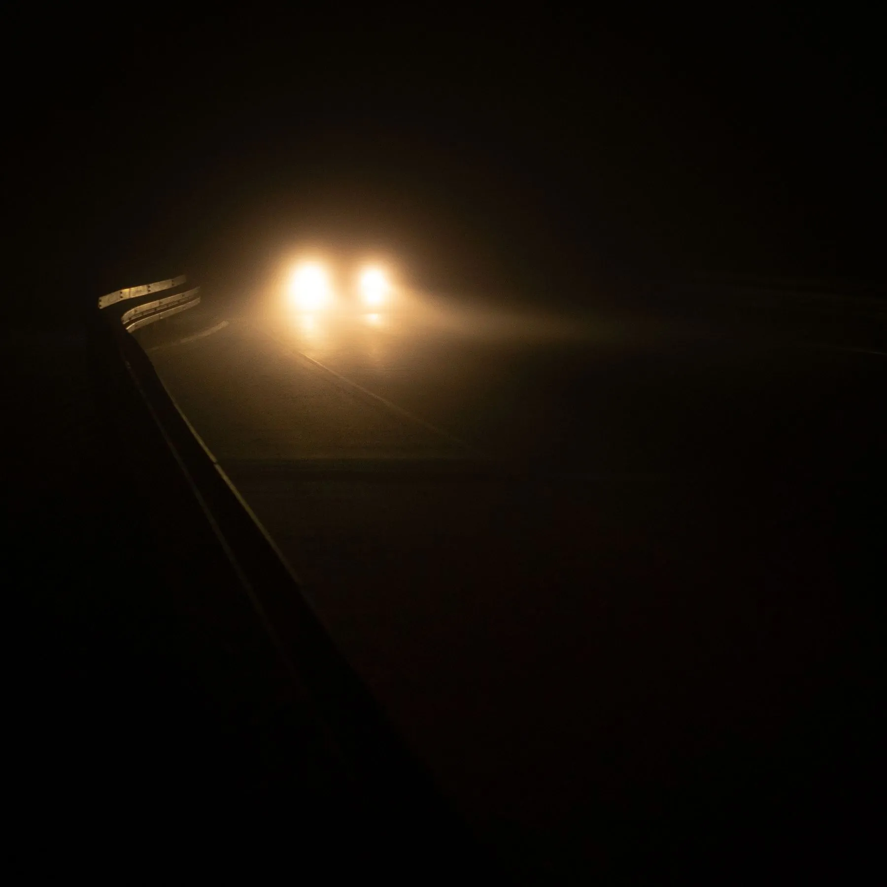 Headlights cutting through fog on a dark road