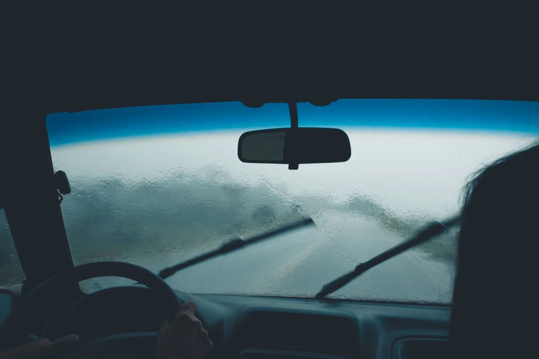 Rain beading on a windshield with the wipers mid sweep, seen from the driver seat